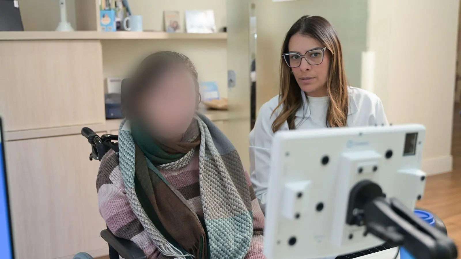 Paciente em cadeira de rodas utiliza o terminal de comunicação alternativa Conversia ao lado de fonoaudióloga do Serraville