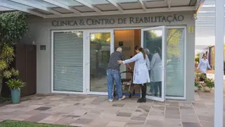 Profissional do Serraville acompanha paciente com andador na entrada do centro de reabilitação