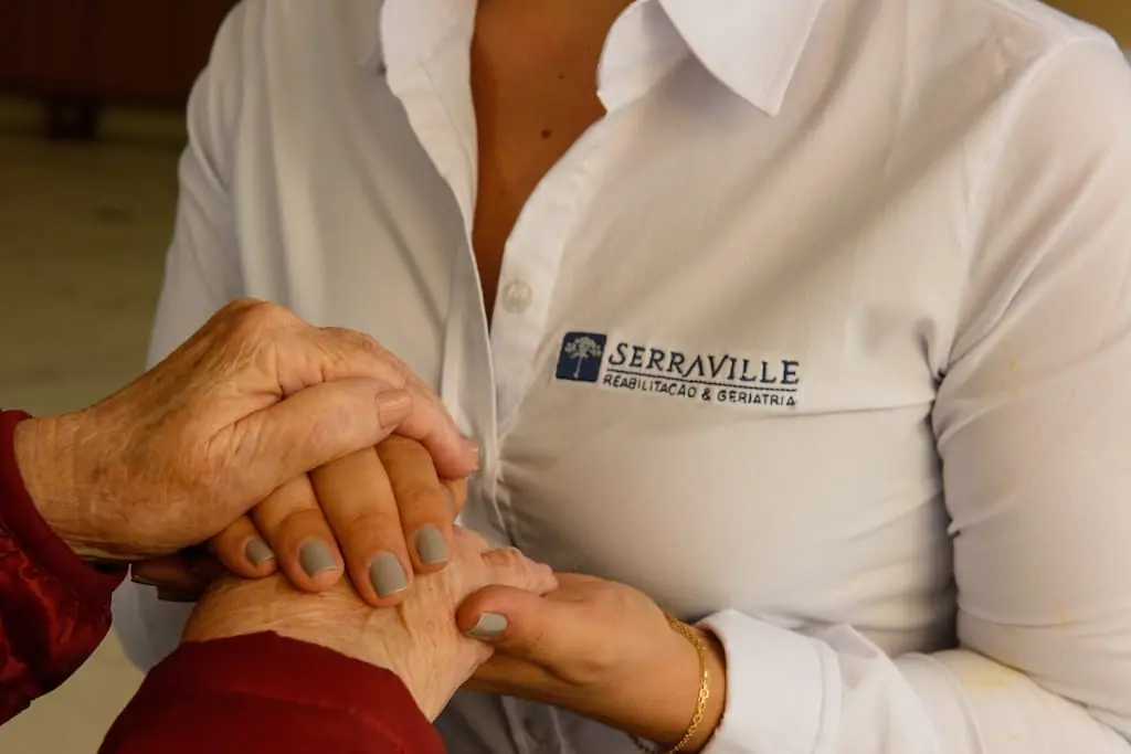 Profissional do Serraville segurando as mãos de uma pessoa idosa, representando apoio ao cuidador familiar.